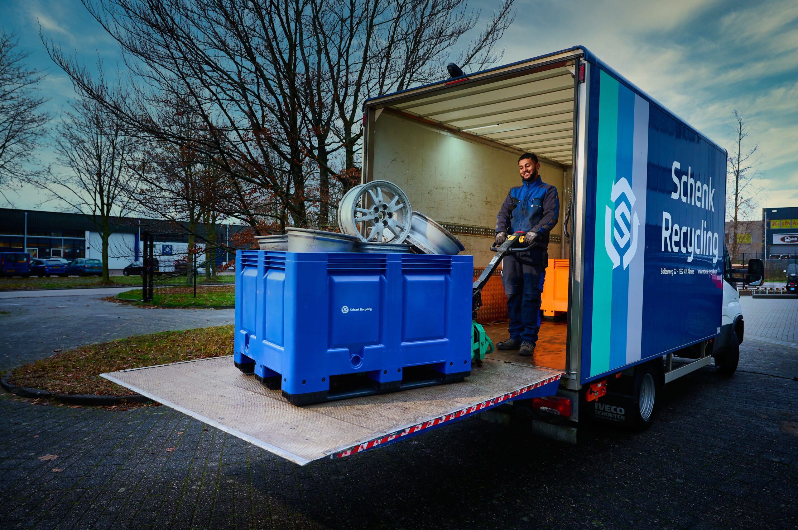 Zakelijke ophaalservice Schenk Recycling Almere Medewerker van Schenk Recycling laadt een blauwe stapelbak met oude velgen in de ophaalbus met laadklep in Almere.