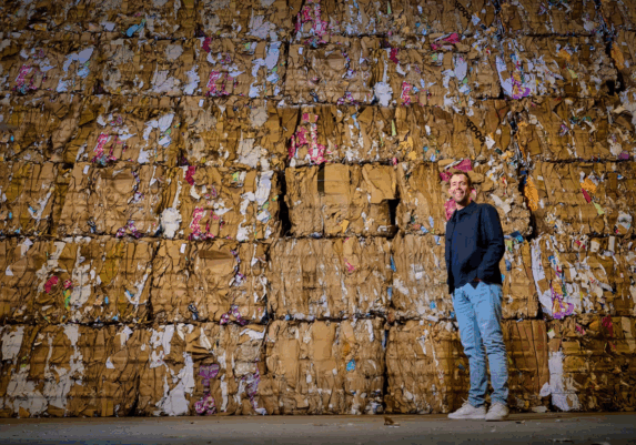 Joost Schenk staat voor gestapelde balen oud papier in de loods van Schenk Recycling.