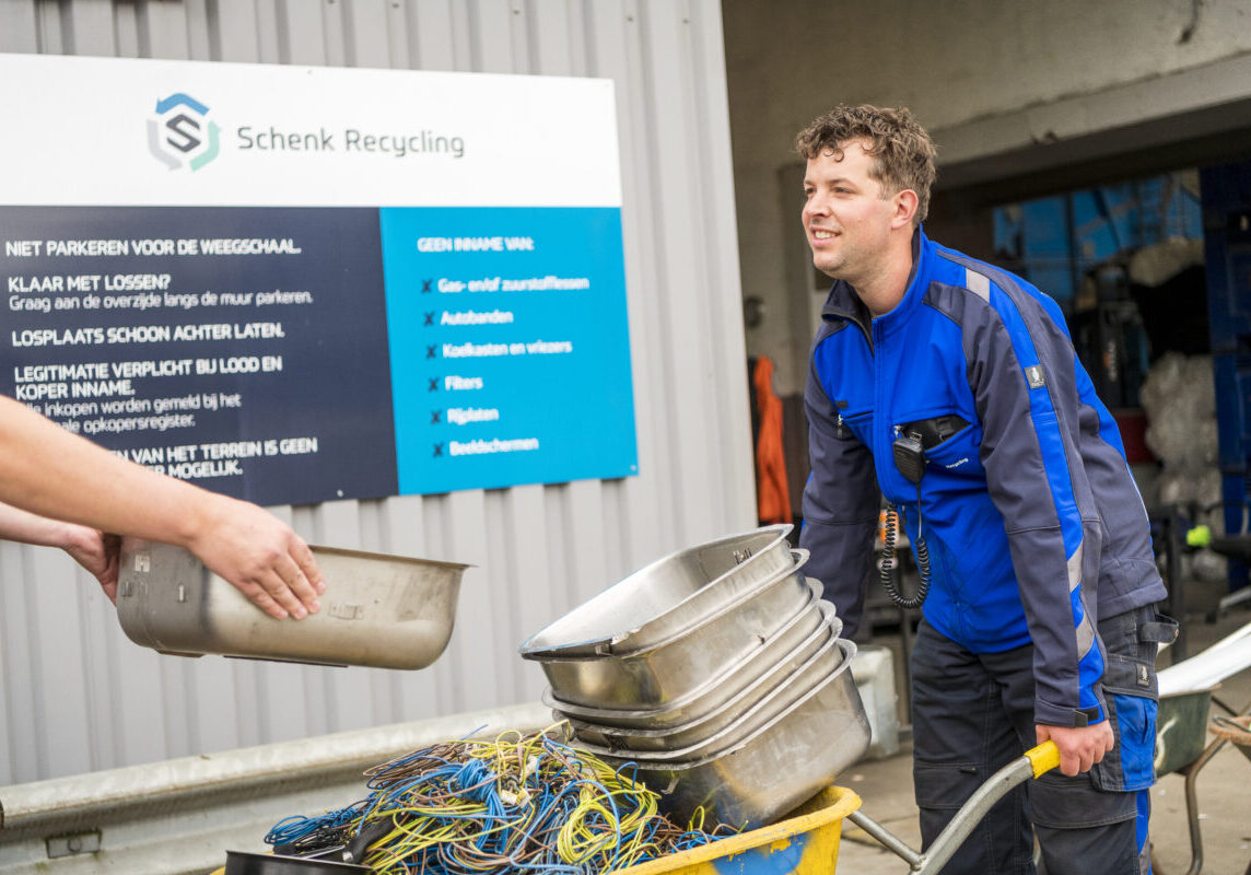 Een medewerker van Schenk Recycling weegt een kruiwagen vol roestvrij staal en ijzer op een geijkte weegschaal.