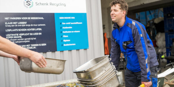 Een medewerker van Schenk Recycling weegt een kruiwagen vol roestvrij staal en ijzer op een geijkte weegschaal.
